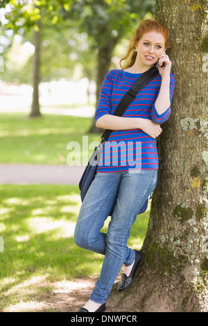 Redhead student leaning against a tree talking on the phone Stock Photo