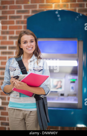 Pretty student standing smiling at camera at the atm Stock Photo