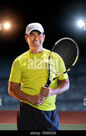 Portrait of Hispanic senior player holding racket standing on tennis court Stock Photo