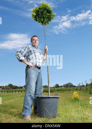 Young man posing with potted oak tree ready for planting in the ground