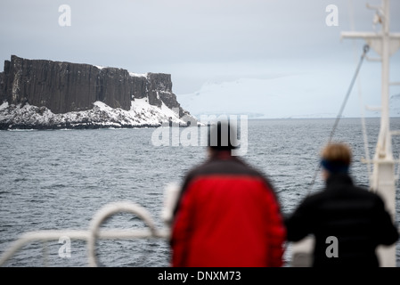 ANTARCTICA - Two passengers stand on the deck of an Antarctic cruise ship to look at the first land sighted after crossing Drake's Passage. The island in the distance is part of the South Shetland Islands along English Strait and Robert Island just off the Antarctic Peninsula. Stock Photo