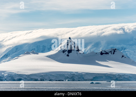ANTARCTICA - A steep peak rises above the surround mountain, while in the background clouds obscure an even taller mountain range in the Gerlache Strait on the Antarctic Peninsula. Stock Photo