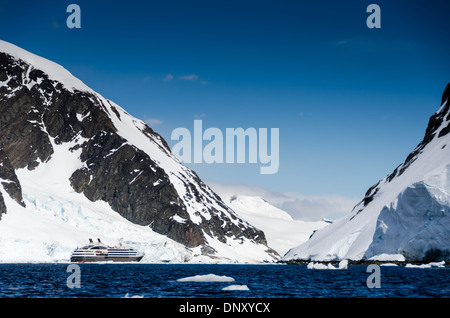 ANTARCTICA - A large luxury French cruise ship, the L'Austral, heads through a narrow channel between mountains on the Antarctic Peninsula (left) and Cuverville Island (right). Stock Photo