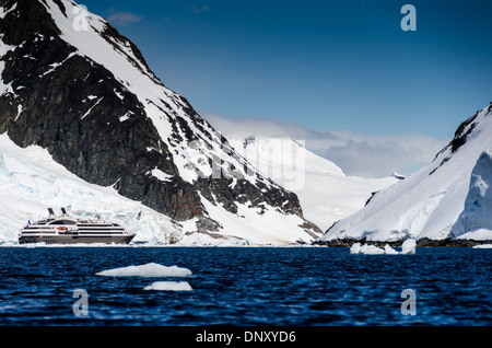 ANTARCTICA - A large luxury French cruise ship, the L'Austral, heads through a narrow channel between mountains on the Antarctic Peninsula (left) and Cuverville Island (right). Stock Photo