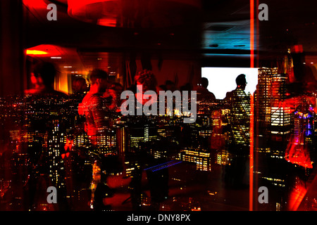 People at a nightime event in a tower block office in Liverpool Street with the city of London in the background. Stock Photo