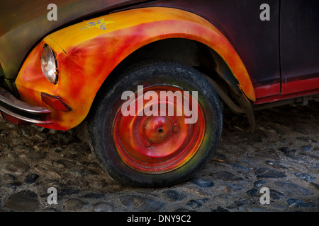 Brightly painted orange & yellow 2CV French car wheel on cobbled street, France Stock Photo