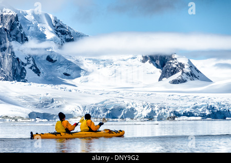 PETERMANN ISLAND, Antarctica — Kayakers paddle through glassy, mirror-like waters along the scenic mountainous shoreline near Petermann Island on the western side of the Antarctic Peninsula. The calm conditions offer perfect reflections of the snow-capped peaks, creating a stunning symmetry between sky and sea in this pristine polar landscape. Stock Photo