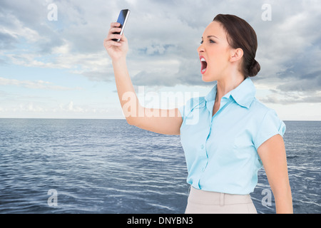 Composite image of angry classy businesswoman yelling at her smartphone Stock Photo