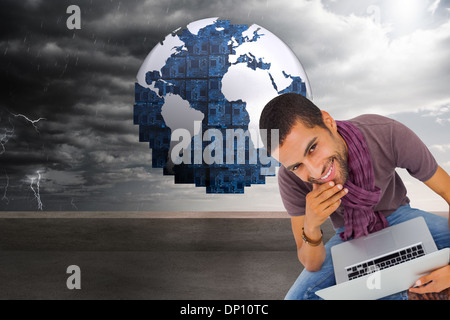 Composite image of thoughtful man sitting on floor using laptop and smiling at camera Stock Photo