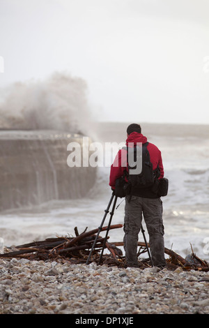 A photographer takes pictures of winter waves crashing over the Cob in Lyme Regis. Stock Photo