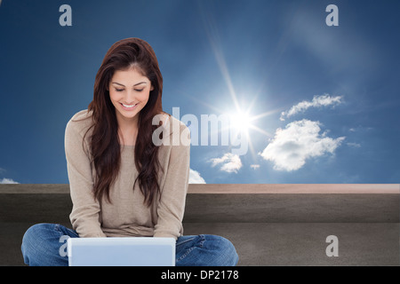 Composite image of brunette sitting on floor using laptop Stock Photo