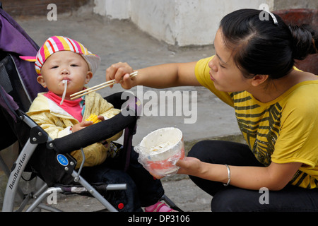 Mother feeding her baby noodles, Xingping, Guangxi, China Stock Photo