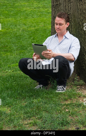 A man leaning against a tree holding an iPad 3g 64gb Stock Photo
