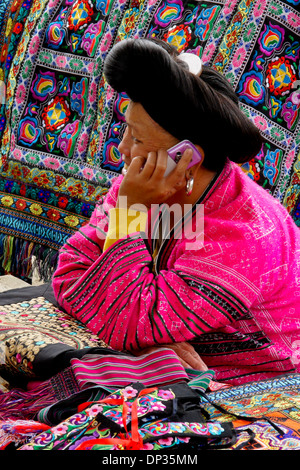 Woman of Red Yao ethnic minority talking on cell phone at handicraft stall, Longsheng (Longji), Guangxi, China Stock Photo