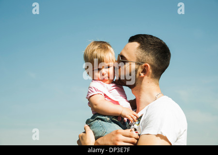 Father Kissing Baby Daughter on Cheek Outdoors, Mannheim, Baden-Wurttemberg, Germany Stock Photo