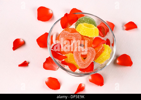 Colored candies with two red hearts in glass bowl and rose petals, top view Stock Photo