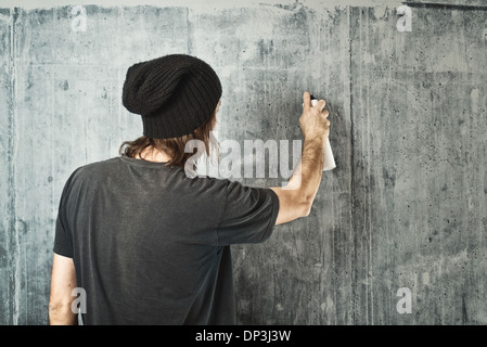 Graffiti artist in black clothes spraying the wall/ Stock Photo