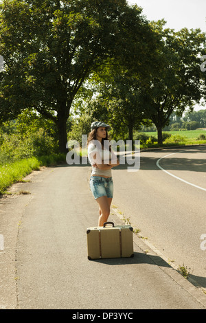 Teenaged girl standing on the side of the road with suitcase, in summer, Germany Stock Photo