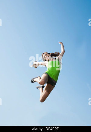 Teenaged girl jumping in mid-air against blue sky, Germany Stock Photo