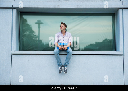 Young man sitting on ledge outdoors, Germany Stock Photo