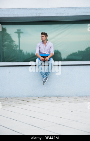 Young man sitting on ledge outdoors, Germany Stock Photo