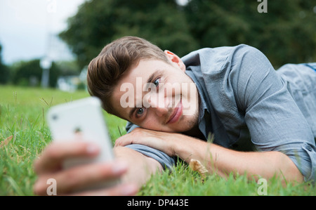 Close-up of young man lying on grass, looking at cell phone, Germany Stock Photo