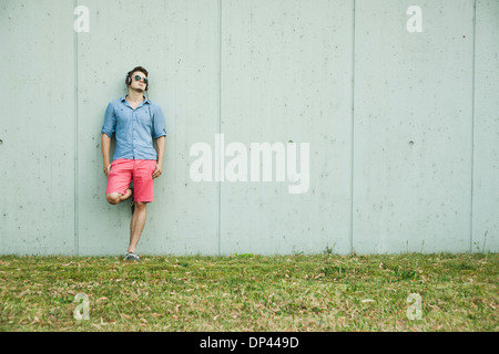 Young man leaning on wall of building, wearing headphones and sunglasses, Germany Stock Photo