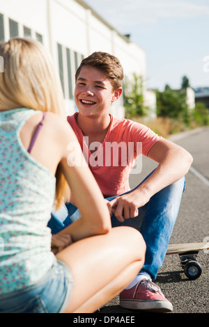 Teenage girl and teenage boy sitting on street, talking, Germany Stock Photo