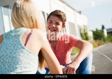 Teenage girl and teenage boy sitting on street, talking, Germany Stock Photo