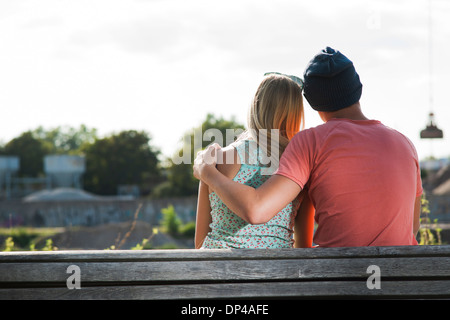 Backview of teenage boy with arm around teenage girl, sitting on bench outdoors, Germany Stock Photo