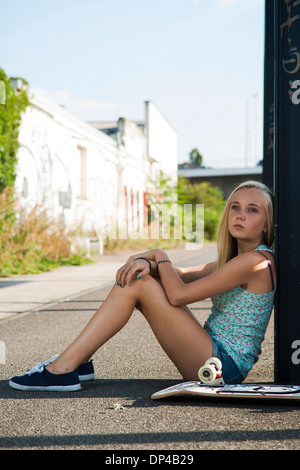 Portrait of teenage girl outdoors with skateboard, looking into the distance, sitting on street, Germany Stock Photo