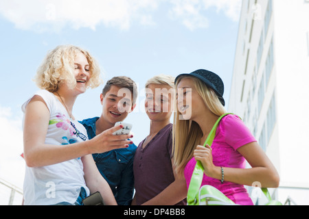 Group of teenagers standing outdoors looking at cell phone and talking, Germany Stock Photo