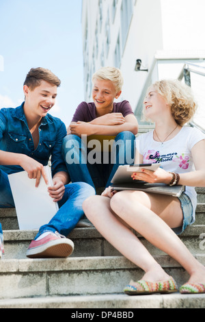 Teenagers sitting on stairs outdoors, talking and looking at tablet computer, Germany
