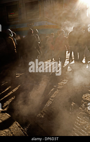 Pedestrians in New York cross a road as steam rises from vents and a low winter sun casts long shadows. Stock Photo