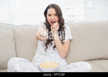 Pretty woman in pyjamas having popcorn while watching scary movie Stock Photo