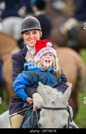 A horse rider gives her daughter a ride at a Christmas meeting of the Beaufort Hunt in Didmarton, Gloucestershire UK on Saturday Stock Photo