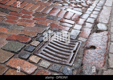 Wet drainage cover on stone pavement of urban road Stock Photo