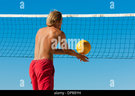 Group of friends - here two women and a man - playing beach volleyball, one in front having the ball Stock Photo