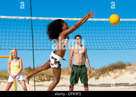 Group of friends - here two women and a man - playing beach volleyball, one in front having the ball Stock Photo