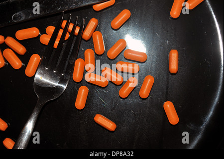A black dinner plate covered in bright orange pills. Stock Photo