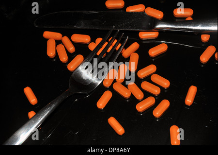 A black dinner plate covered in bright orange pills. Stock Photo