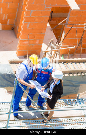Team or architect and builder or worker with helmets discuss on a scaffold construction plan or blueprint or checklist Stock Photo