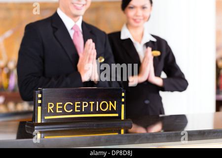 Chinese Asian reception team at luxury hotel front desk welcoming guests with typical gesture, a sign of good service Stock Photo