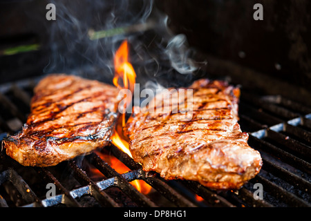 Beef steaks cooking in open flame on barbecue grill Stock Photo