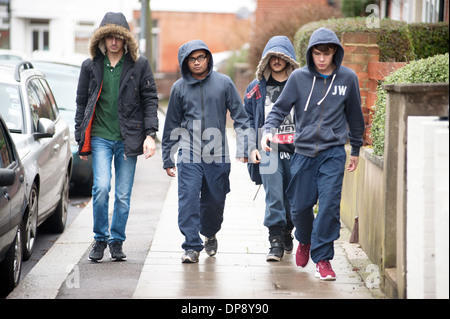 A group of teenage boys in hoodies walking together down a suburban street. Stock Photo