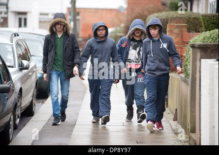 A group of teenage boys in hoodies walking together down a suburban street. Stock Photo