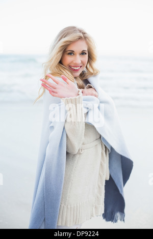 Happy blonde woman in a blanket waving at the camera Stock Photo