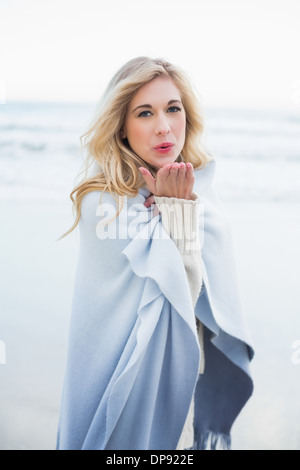 Cute blonde woman in a blanket blowing a kiss to the camera Stock Photo