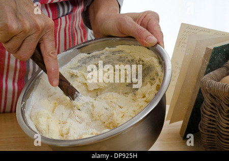 Hands stirring cake mix with wooden spoon next to recipe book. Stock Photo