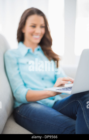 Smiling gorgeous brunette sitting on sofa using laptop Stock Photo